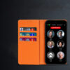The RAZ Memory Cell Phone is shown in an orange wallet-style case that includes three card slots on the inside flap, each holding a credit card. The phone’s screen displays six large contact buttons with names and photos—Cindy Miller, Michael, Peter Stevens, Anne Peters, Linda Smith, and Cathy Clark—along with a red “EMERGENCY” button at the top.