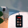 Photo of a RAZ Memory Cell Phone charging on a white table. The phone is on the Wireless Charging Pad, which is connected to a wall outlet with a black charging cable. The screen displays six large contact buttons with names and photos—Cindy Miller, Jeff, Peter Stevens, Anne Peters, Linda Smith, and Cathy Clark—and a prominent red "EMERGENCY 911" button at the top. The phone status bar shows a 73% battery level, time (3:22 PM), day (TUE), and 4G signal strength. A green plant is partially visible on the left side of the image.